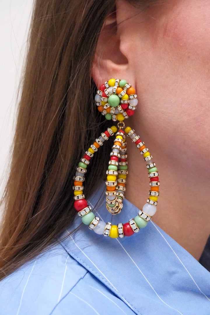 Boucles d'Oreilles en perles multicolore vert, jaune, rouge, orange et blanc et pendantes avec un fermoir clip portées à l'Oreilles d'une femme
