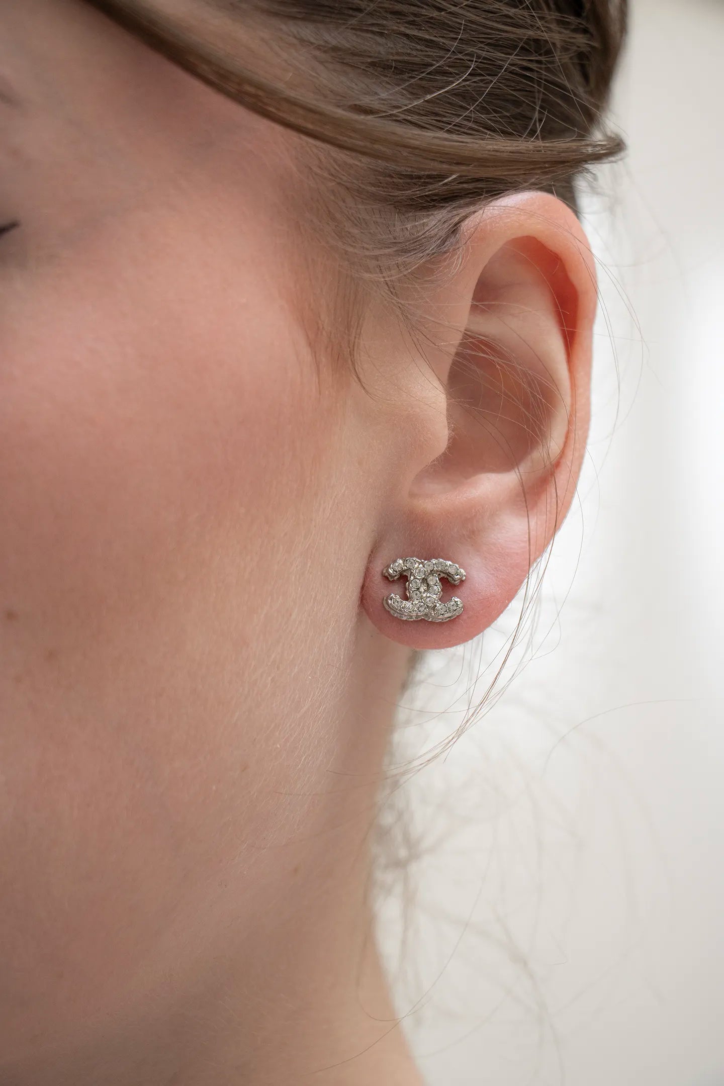 Petite Paire de boucles d'oreilles CC portée Chanel vintage, strass étincelants sur monture argentée texturée.