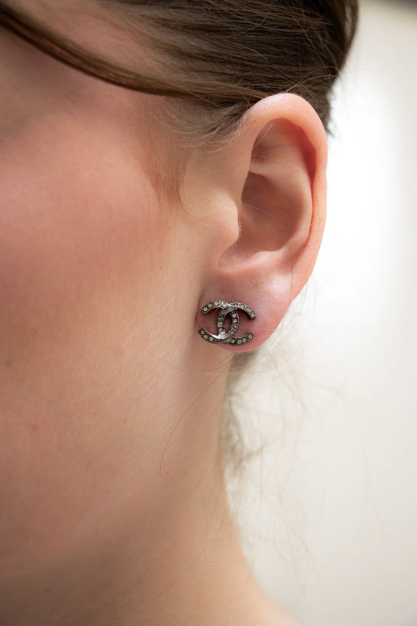 boucles d'oreilles CC portée ornée des strass sertis vintage Chanel, éclat contrasté et raffinement intemporel.