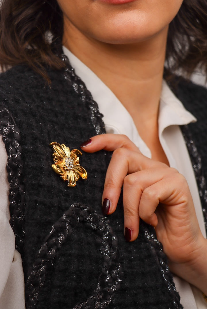 détail d'une Petite broche dorée en forme de fleur et détail de strass sur un veston noir