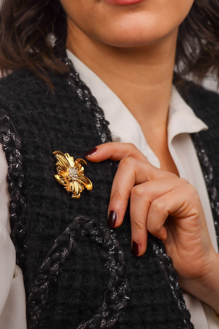 détail d'une Petite broche dorée en forme de fleur et détail de strass sur un veston noir