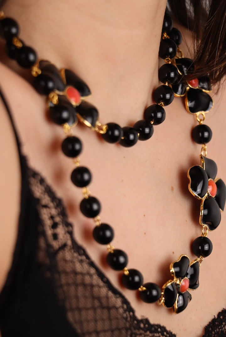 Détail d'un Collier long en perles noires et motif trèfles à quatre feuille noir centre rouge corail détail doré