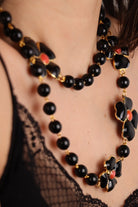 Détail d'un Collier long en perles noires et motif trèfles à quatre feuille noir centre rouge corail détail doré