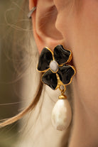 Femme portant des boucles d'oreilles pendantes trèfle noir et perle blanche nacré, allure parisienne sophistiquée
