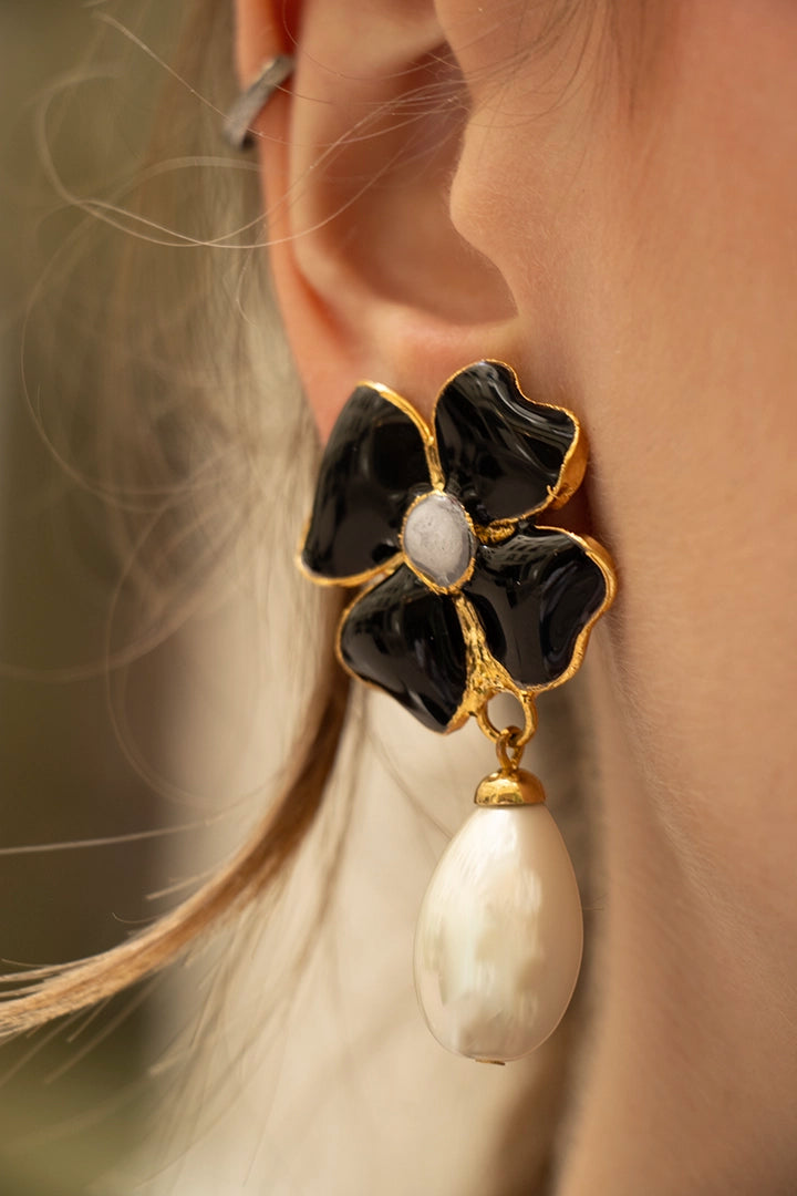 Femme portant des boucles d'oreilles pendantes trèfle noir et perle blanche nacré, allure parisienne sophistiquée
