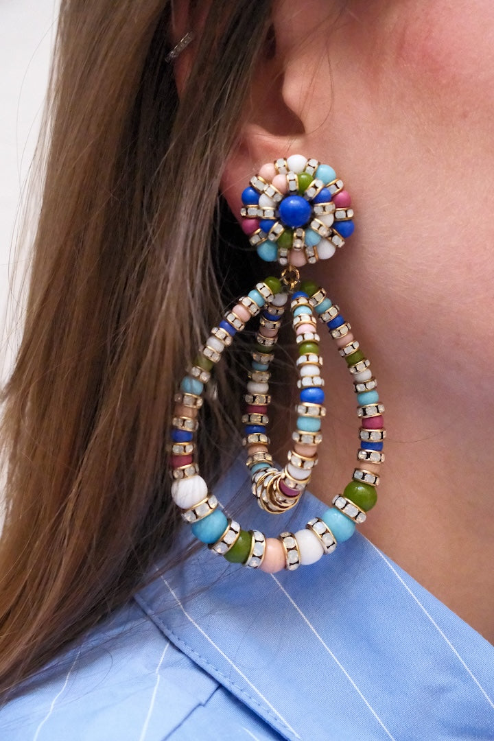 Boucles d'Oreilles en perles multicolore bleu, vert, rose et turquoise large et pendantes avec un fermoir clip portées à l'oreilles d'une femme