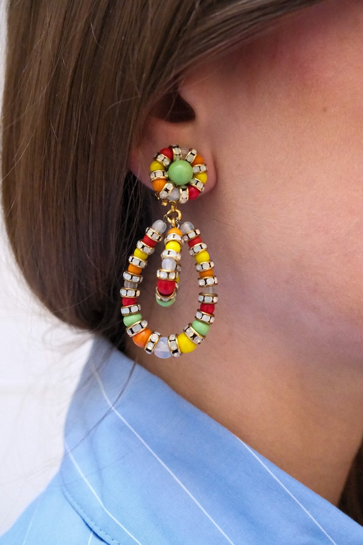 Petite paire de Boucles d'Oreilles en perles multicolore vert, jaune, rouge, orange et blanc et pendantes avec un fermoir clip portées à l'oreille par une femme