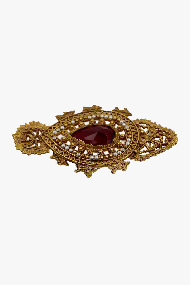 Broche vintage dorée avec détail centrale  d'une pierre rouge et ornée de petites perles blanches 