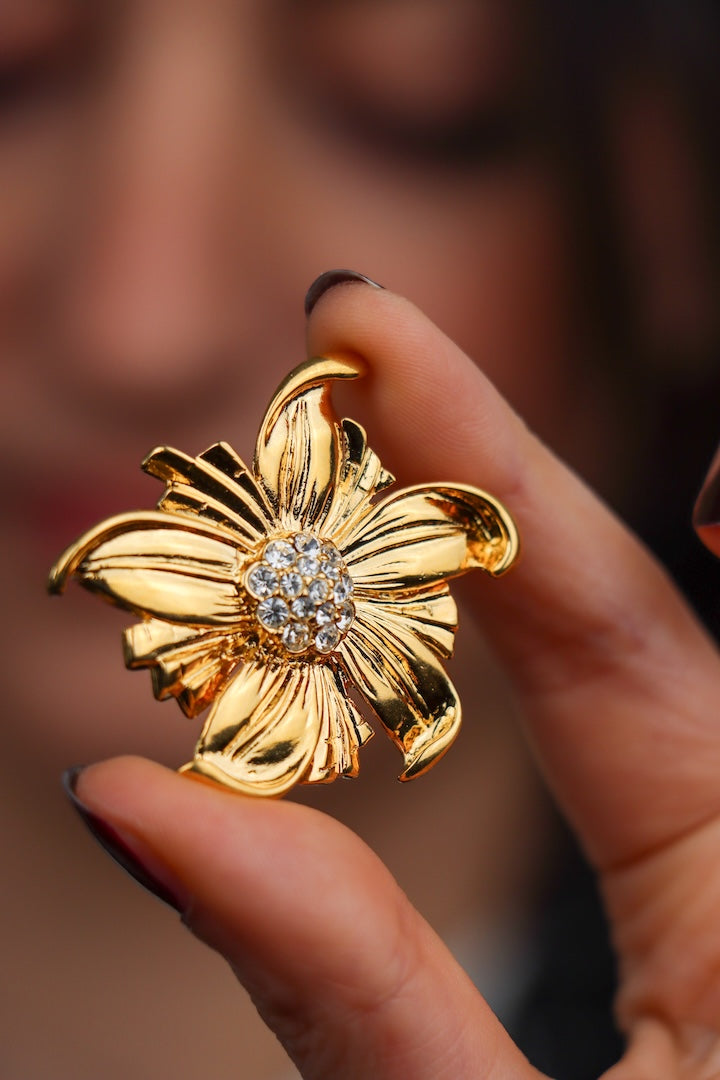 Petite broche dorée en forme de fleur et détail de strass vu de près 