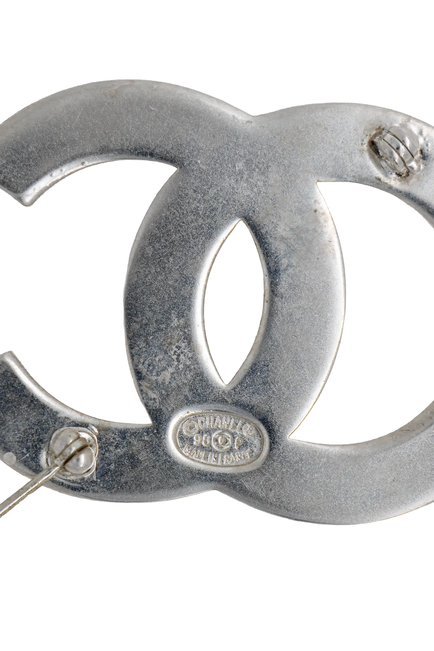 Gros plan sur le poinçon Chanel 98 CC P et le système d'attache, détail artisanal du métal argenté.