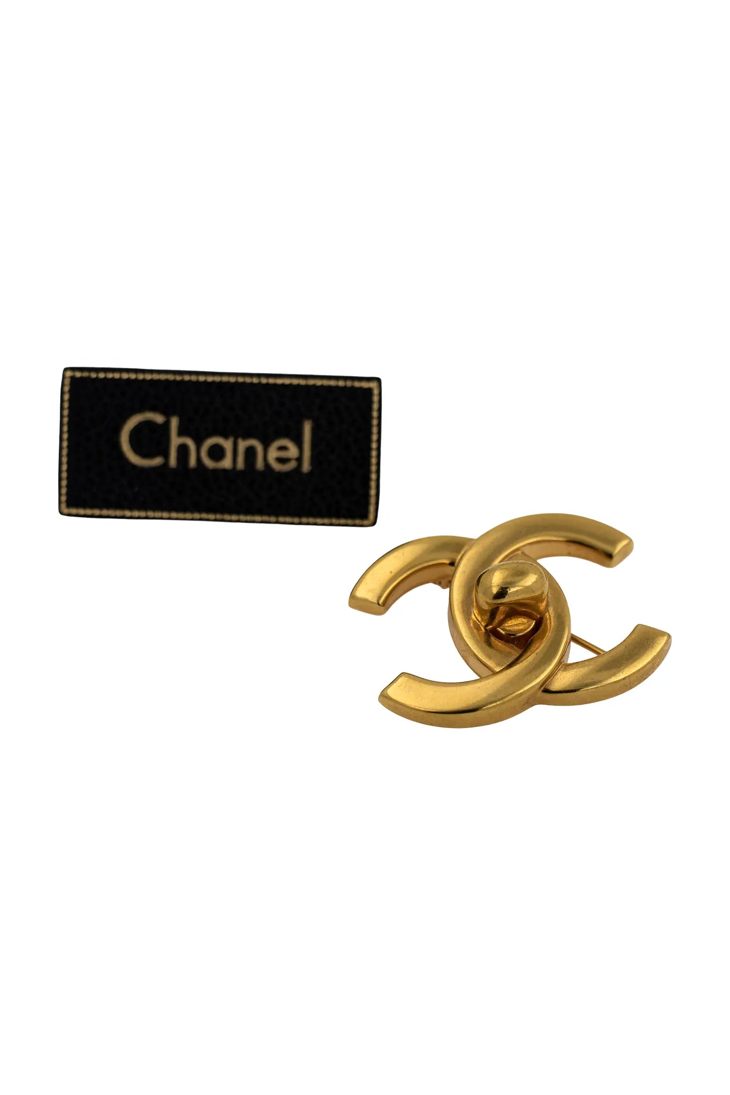 Broche Chanel vintage dorée présentée avec son étiquette noire et dorée, gage d'authenticité et d'héritage.