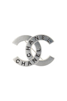 Broche Chanel vintage argentée, monogramme CC ajouré gravé du mot Chanel, éclat sophistiqué intemporel.