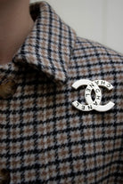 Broche Chanel vintage argentée portée sur col, monogramme CC ajouré gravé du mot Chanel, éclat sophistiqué intemporel.