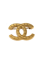 Broche Chanel vintage dorée présentée avec son étiquette noire et dorée, gage d'authenticité et d'héritage.