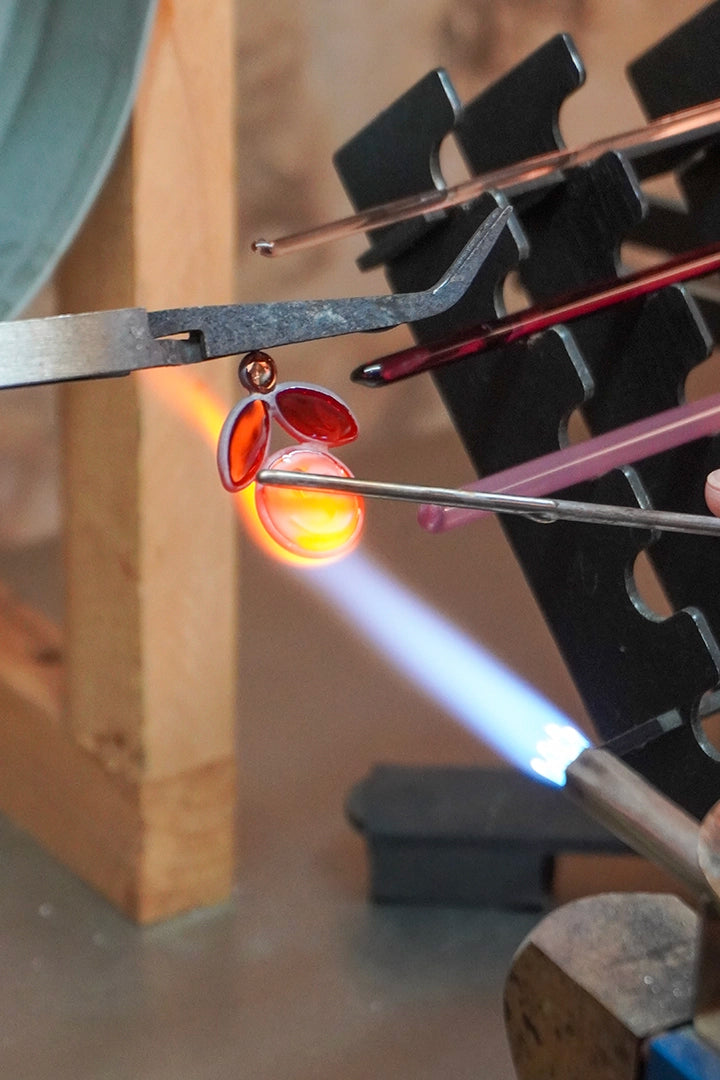 Artisan Françoise Montague façonnant à la flamme une boucle d'oreille Emma en pâte de verre, atelier Paris