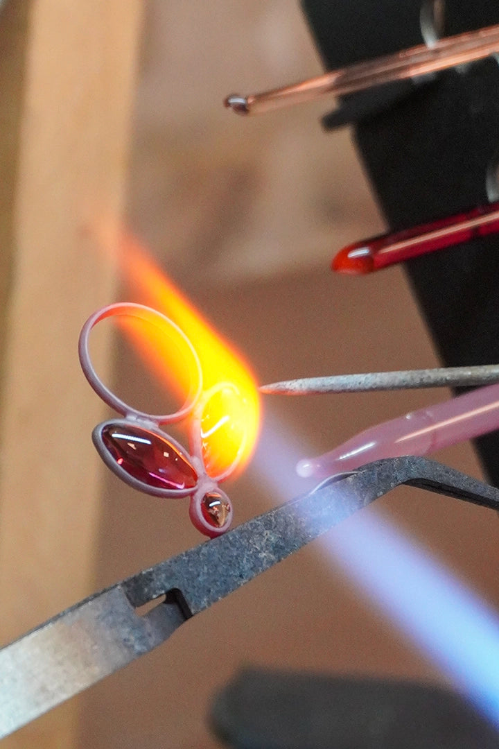 Geste artisanal au chalumeau sur une perle de verre incandescente, savoir-faire haute couture transmis depuis 1945